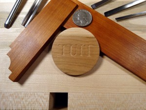 photo #1 of a "round tuit" carving. This side shows the word "TUIT" carved on a disc shape.